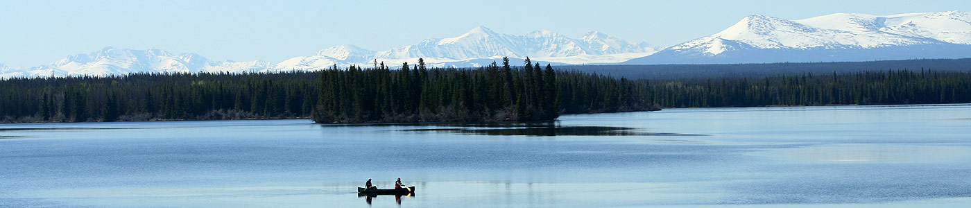 Two people paddle a canoe on Nimpo Lake with snowy mountains behind.
